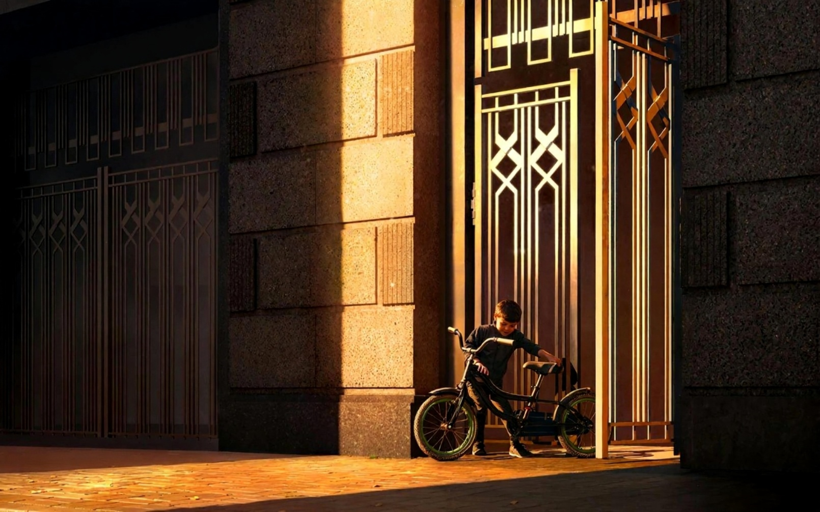 Художественное фото с ребенком на велосипеде у входа в здание с красивой архитектурной подсветкой в золотых тонах